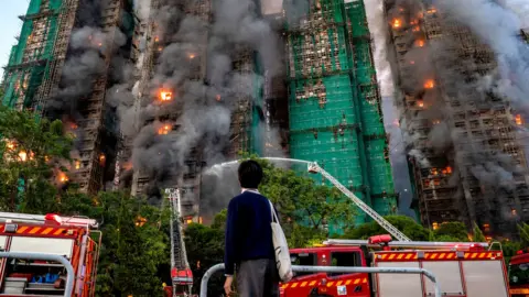 Shutterstock A student watches as smoke and flames rise as a major fire engulfs several residential buildings at Wang Fuk Court
Single use only on this story, can be syndicated