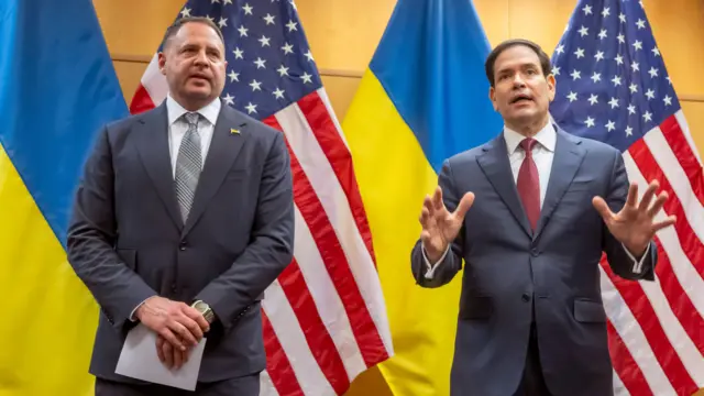 Yermak and Rubio - both wearing suits - stand next to one another, flanked by US and Ukrainian flags