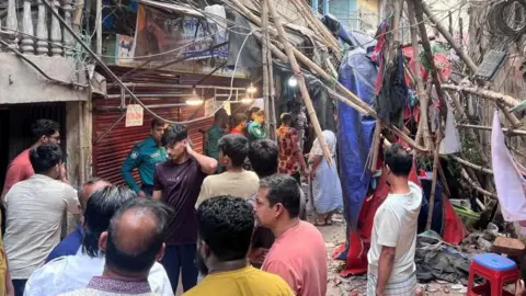 Reuters People gather in an alley looking at damage to scaffolding following an earthquake in Dhaka.