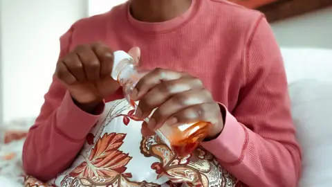 Getty Images A black woman in bed holding a bottle of cough mixture