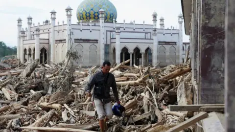 Reuters  A man walks through a village destroyed by flooding